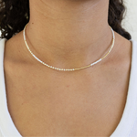 Woman wearing a delicate white seed bead necklace that has gold accent beads.