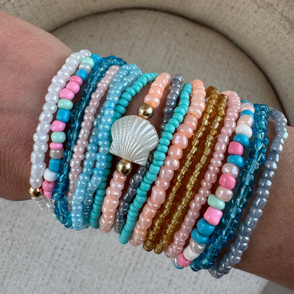 Picture of a woman's wrist wearing 16 different bracelets in Beach themed colors.  Bracelets are shades o white, corals, pinks, blues and amber.