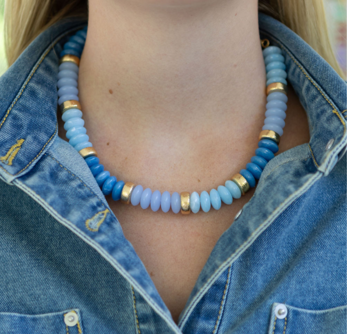 Chunky blue beaded necklace with gold accents worn by a person in a denim jacket.