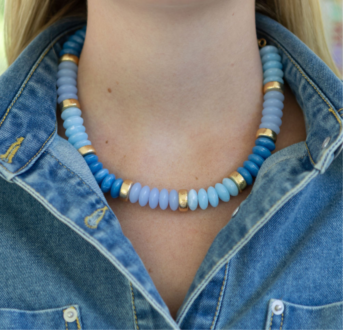 Chunky blue beaded necklace with gold accents worn by a person in a denim jacket.