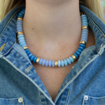 Chunky blue beaded necklace with gold accents worn by a person in a denim jacket.
