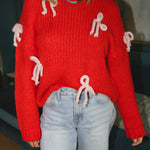 Woman wearing a red knitted sweater with white yarn bows attached and a blue/green beaded necklace
