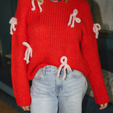 Woman wearing a red knitted sweater with white yarn bows attached and a blue/green beaded necklace