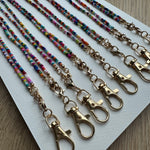 Picture of 8 multicolored beaded lanyards with gold clasps lined up next to each other.