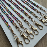 Picture of 8 multicolored beaded lanyards with gold clasps lined up next to each other.