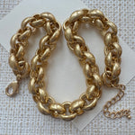 Chunky gold chain necklace on a textured white background