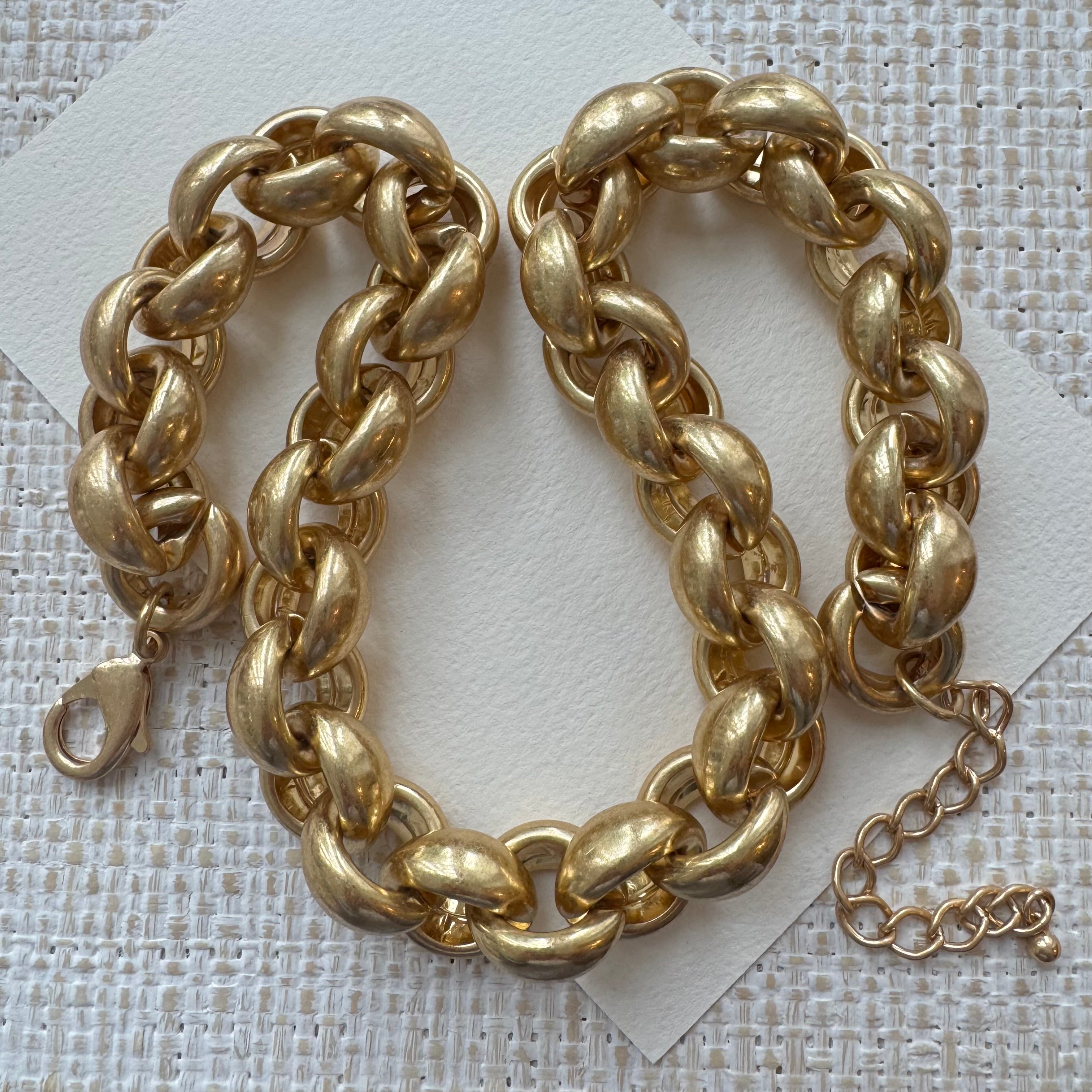 Chunky gold chain necklace on a textured white background