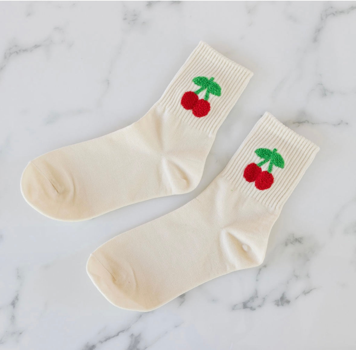 Pair of cream socks with cherry design on a marble background
