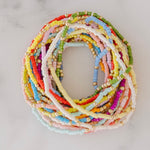 Picture of a stack of tiny beaded bracelets in greens, yellows, blues and pinks.