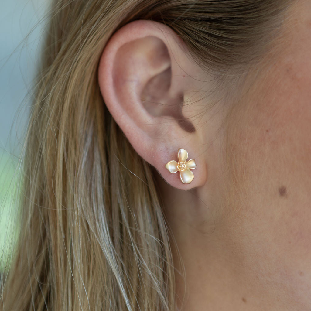 Close-up of an ear wearing a gold flower-shaped earring with blurred background