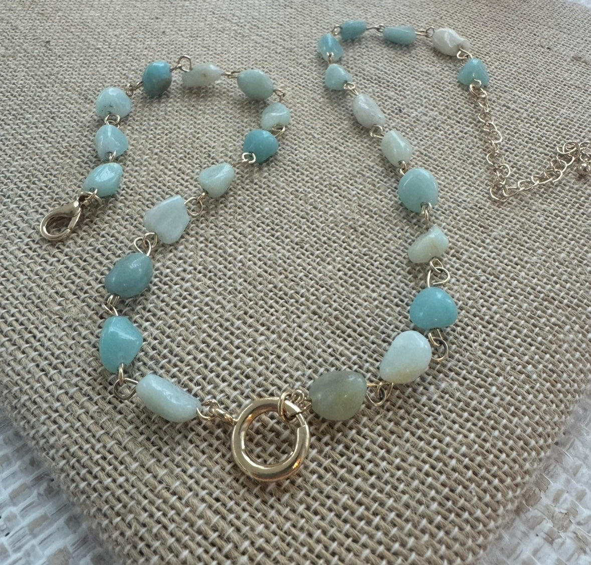 Picture of a necklace made of turquoise colored smooth stone beads with a large gold toggle clasp at its center.