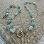 Picture of a necklace made of turquoise colored smooth stone beads with a large gold toggle clasp at its center.