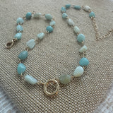 Picture of a necklace made of turquoise colored smooth stone beads with a large gold toggle clasp at its center.