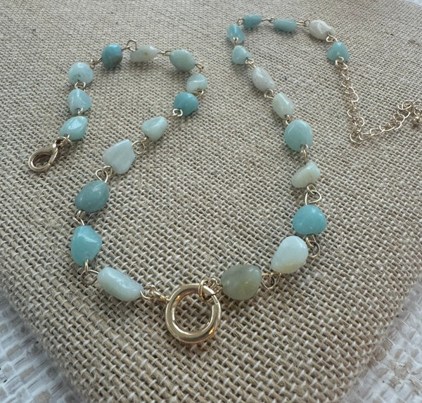 Picture of a necklace made of turquoise colored smooth stone beads with a large gold toggle clasp at its center.