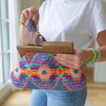 Person putting sunglasses in a clutch with brown at the top and a purple, orange, and yellow colored cloth design 