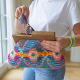 Person putting sunglasses in a clutch with brown at the top and a purple, orange, and yellow colored cloth design 