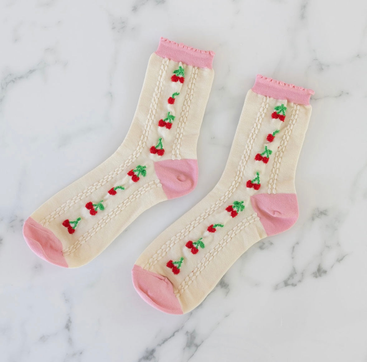 Pair of socks with cherry design and pink edging on a marble background
