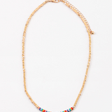 Dainty gold bead necklace with small red, yellow and turquoise beads at its center.