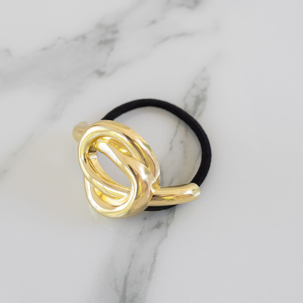 Gold knot-shaped hair accessory on a black hair tie against a marble background
