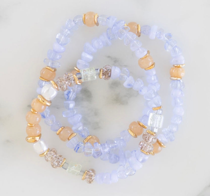 Stack of beaded bracelets with blue, beige, and clear beads on a marble surface