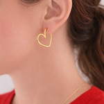 Gold heart-shaped earring worn by a person with a red sweater.