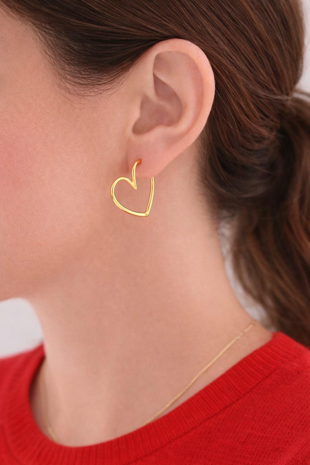 Gold heart-shaped earring worn by a person with a red sweater.