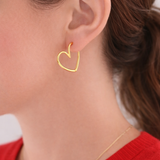 Gold heart-shaped earring worn by a person with a red sweater.