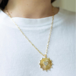 Girl wearing a necklace around her neck with a gold thin chain with a sun/heart medallion attached to it