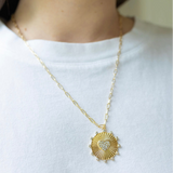 Girl wearing a necklace around her neck with a gold thin chain with a sun/heart medallion attached to it