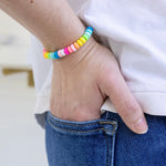 Picture of a woman's hand in her back pocket wearing a bead bracelet in pinks, yellows and blues.