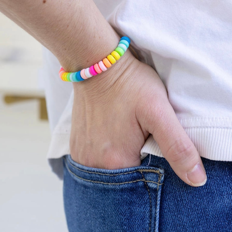 Picture of a woman's hand in her back pocket wearing a bead bracelet in pinks, yellows and blues.