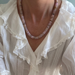 Necklace with pink beads worn by a person in a white blouse with lace details.