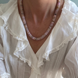 Necklace with pink beads worn by a person in a white blouse with lace details.