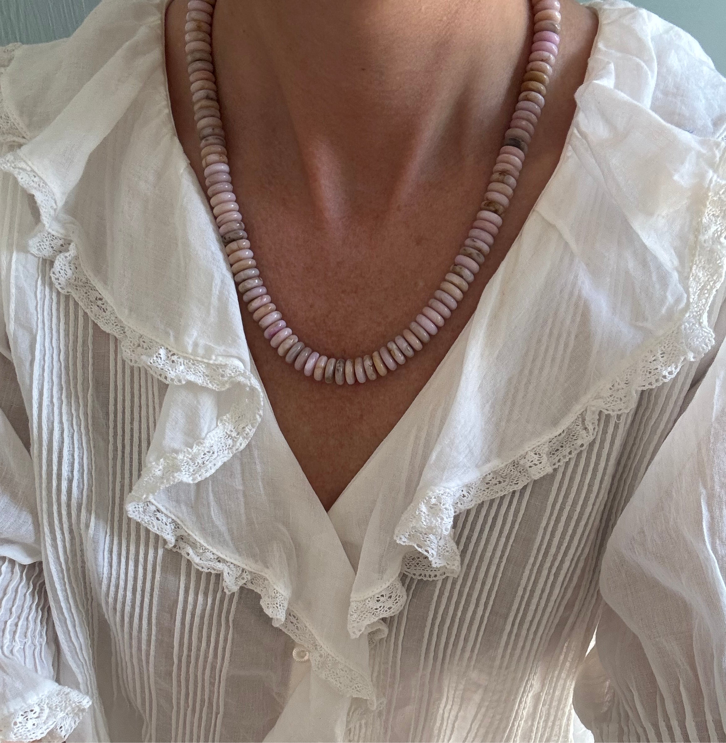 Necklace with pink beads worn by a person in a white blouse with lace details.