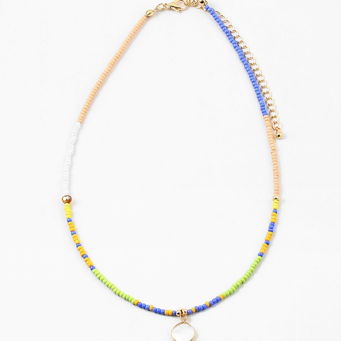 Dainty bead necklace in colors of blue, yellow, tan, green and white. Necklace has a small white disc pendant.