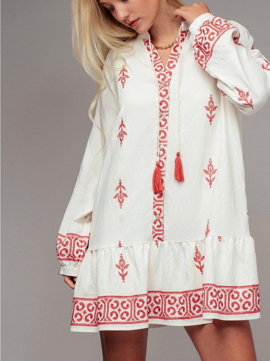 Woman wearing white dress with red embroidery and tassels on a plain background