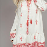 Woman wearing white dress with red embroidery and tassels on a plain background