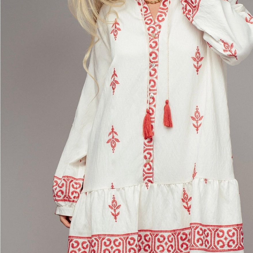 Woman wearing white dress with red embroidery and tassels on a plain background