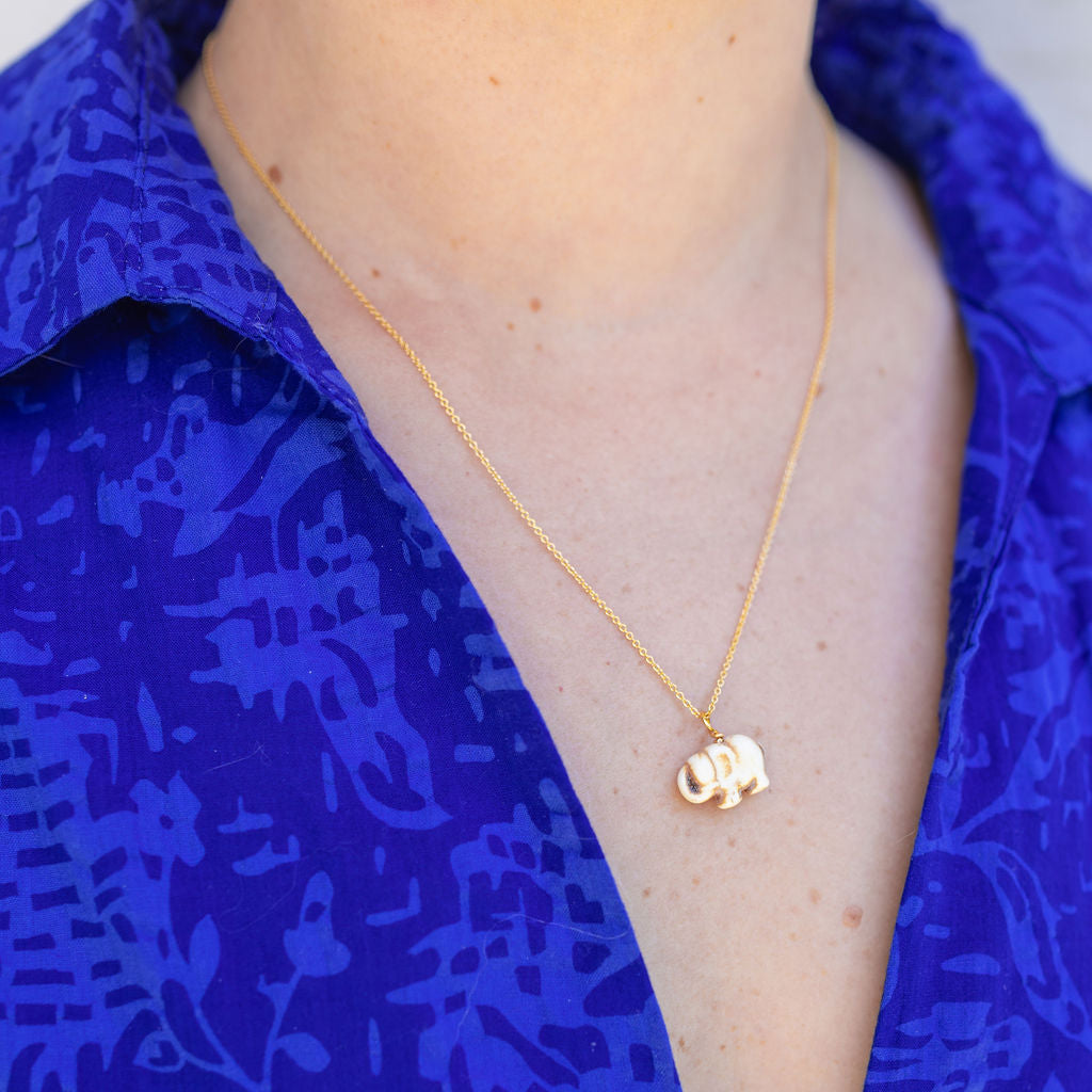Woman wearing a gold chain necklace with a gold elephant attached to it