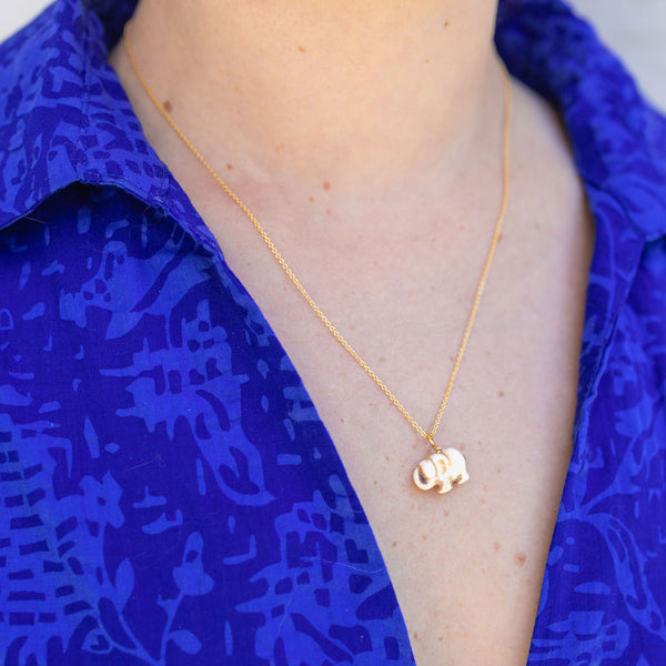 Woman wearing a gold chain necklace with a gold elephant attached to it