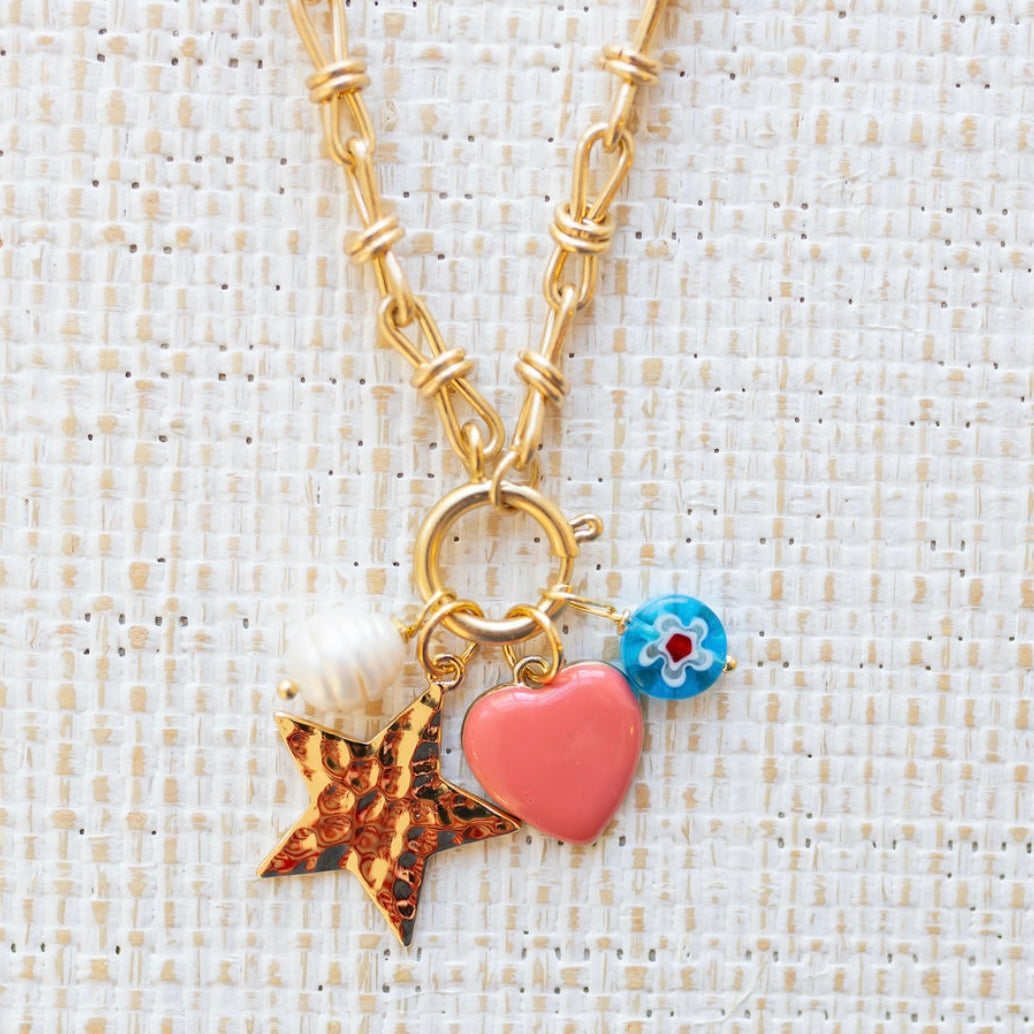 Picture of gold toggle chain with four charms. One is a fresh water pearl, one a gold star, one a pink heart and the other a blue bead with a white flower.