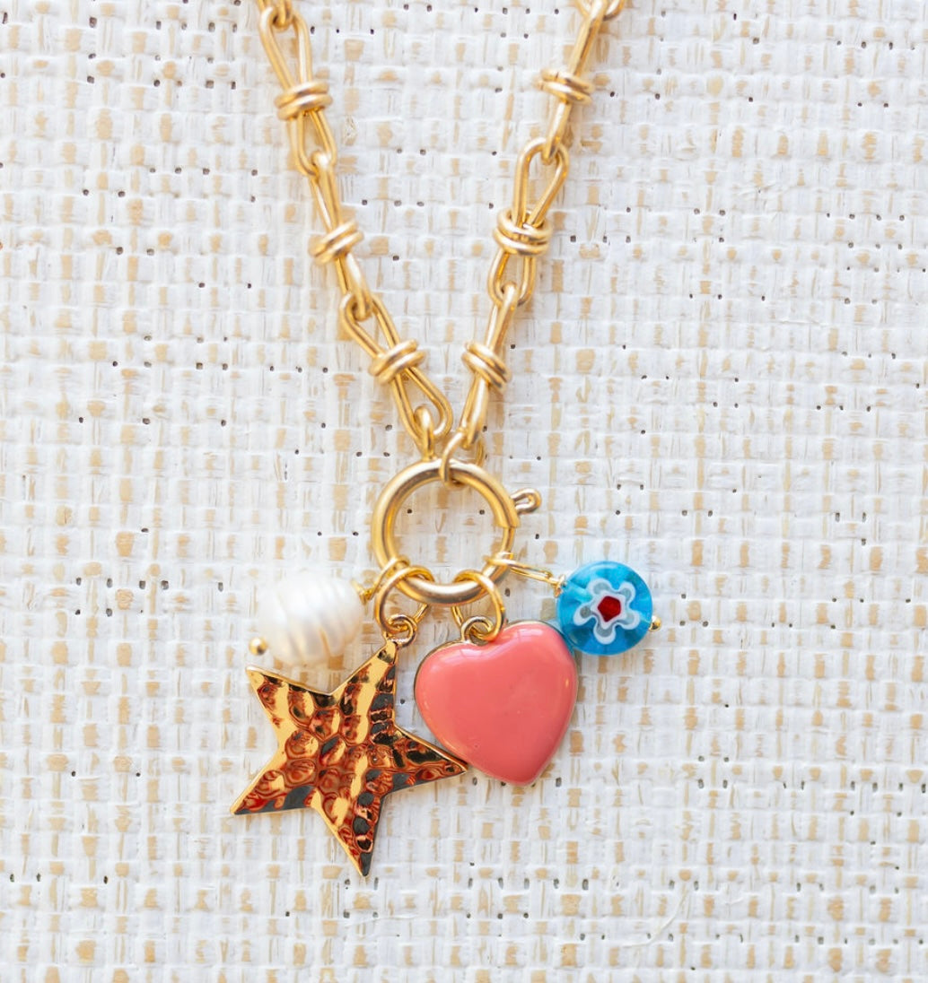 Picture of gold toggle chain with four charms. One is a fresh water pearl, one a gold star, one a pink heart and the other a blue bead with a white flower.