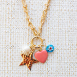 Picture of gold toggle chain with four charms. One is a fresh water pearl, one a gold star, one a pink heart and the other a blue bead with a white flower.