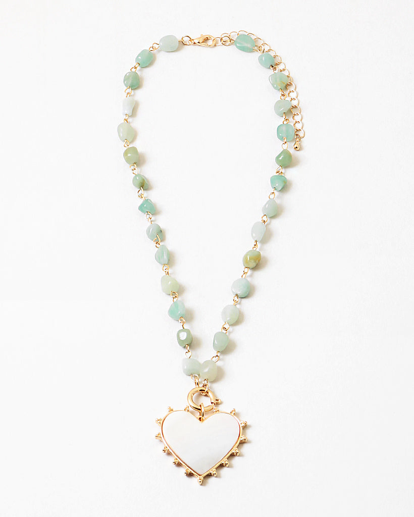 Picture of a necklace made of gold connectors and small light green stones. Necklace has a white enamel heart pendant.