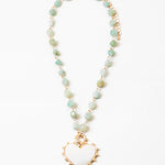 Picture of a necklace made of gold connectors and small light green stones. Necklace has a white enamel heart pendant.