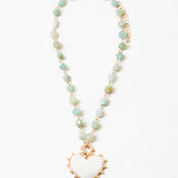 Picture of a necklace made of gold connectors and small light green stones. Necklace has a white enamel heart pendant.