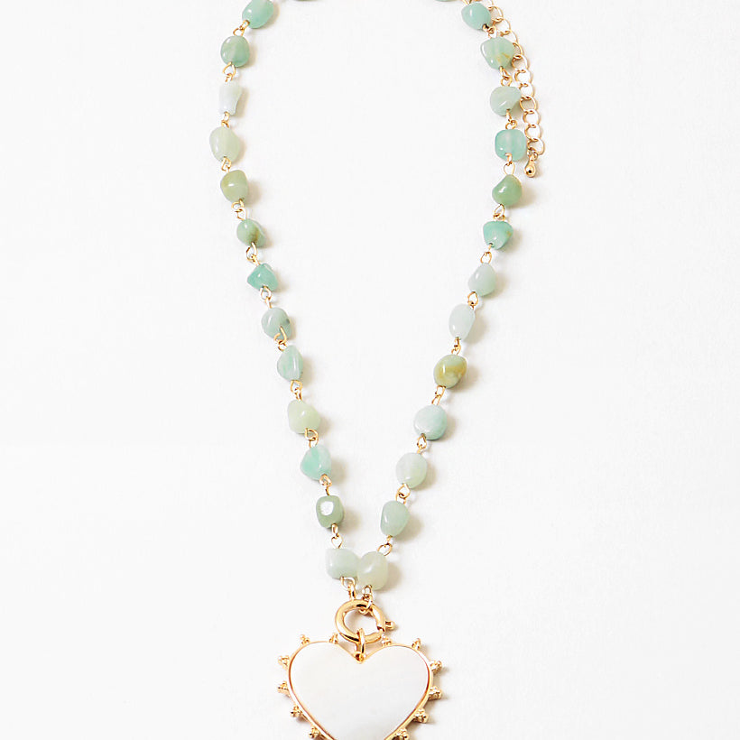 Picture of a necklace made of gold connectors and small light green stones. Necklace has a white enamel heart pendant.