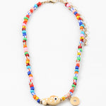 Picture of a bright multi-colored bead necklace with a tan fish bead and a gold disc pendant.