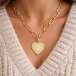 Gold heart-shaped pendant necklace worn by a person in a beige sweater.