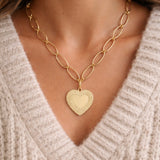 Gold heart-shaped pendant necklace worn by a person in a beige sweater.